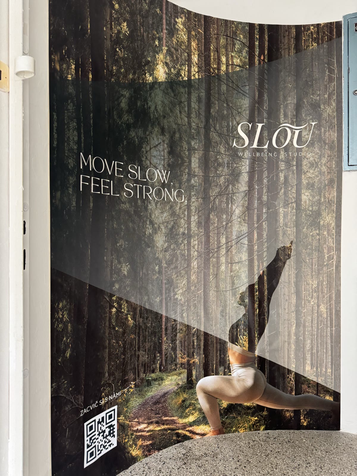 Zahnutý banner Slou pri vchode do štúdia: les, postava v cviku a nápis Move slow, feel strong